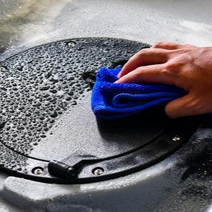 Hand using blue micro-fiber fishing towel to wipe water droplets off black surface, Mojo Surfcasting tool