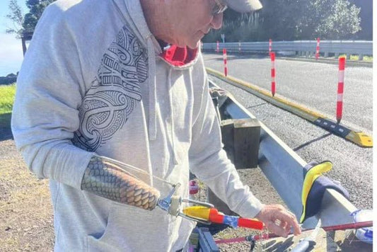 Man in grey hoodie fishing with Mojo surfcasting rod by roadside guardrail in New Zealand